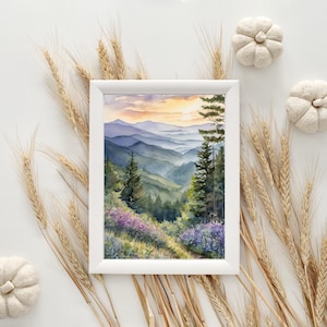Pode incluir: Uma pintura em aquarela emoldurada de uma paisagem de montanha. A obra apresenta camadas de montanhas azuis e verdes sob um c&eacute;u de p&ocirc;r do sol. Flores silvestres roxas e &aacute;rvores perenes em primeiro plano. A moldura &eacute; branca.