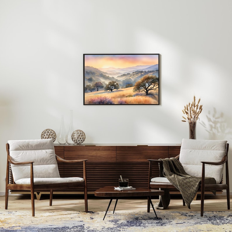 May include: A watercolor painting of a landscape with rolling hills, trees, and a sunset in the background. The painting is framed in a black frame and is hanging on a white wall.