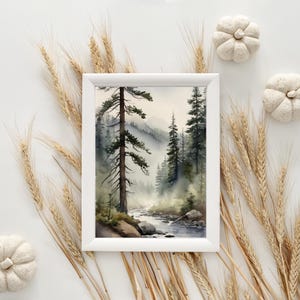 May include: A watercolor painting of a misty forest scene with a river flowing through it. The painting is framed in a white frame and is surrounded by wheat stalks.