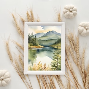 Op de afbeelding: Een ingelijste aquarel schilderij van een serene bergmeersc&egrave;ne. Het kunstwerk, in een witte lijst, toont groene bomen, blauwe bergen en een reflecterende meer. Decoratieve tarwearen en witte pompoenen omringen de lijst.