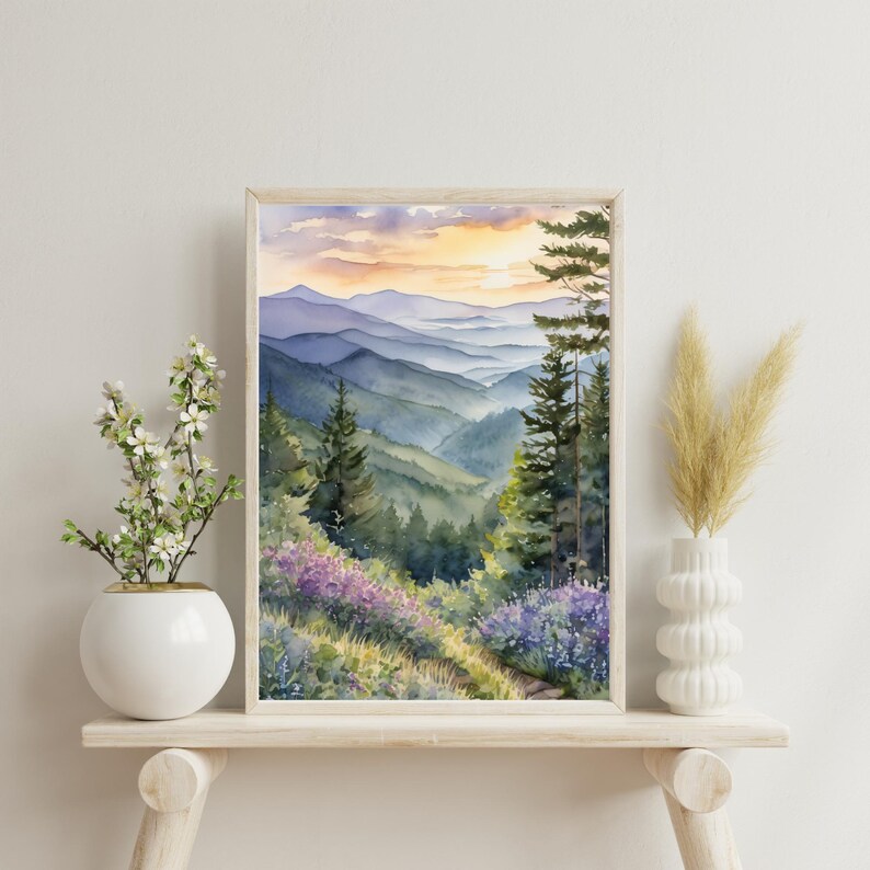 Pode incluir: Pintura em aquarela de uma paisagem de montanha em uma moldura de madeira. A obra retrata camadas de montanhas azuis e verdes sob um c&eacute;u de p&ocirc;r do sol. Flores silvestres roxas e &aacute;rvores perenes est&atilde;o em primeiro plano.