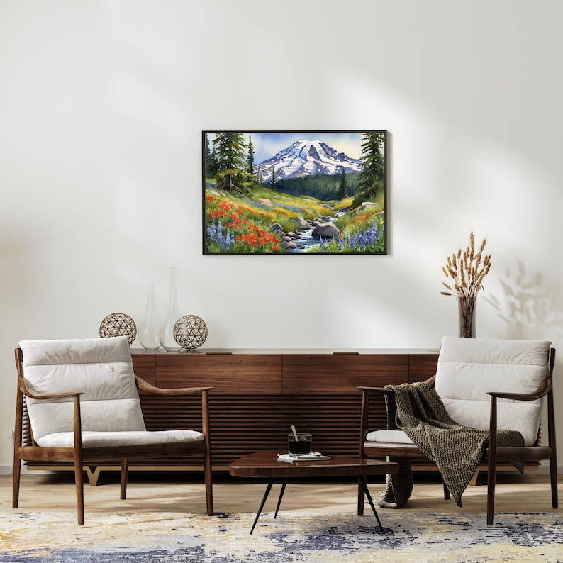 May include: A framed watercolor painting of a mountain scene with a stream running through a field of wildflowers. The mountain is snow-capped and the sky is blue. The painting is framed in black.