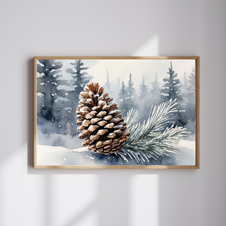 May include: Watercolor painting of a pine cone and evergreen branch in a snowy forest scene. The artwork is framed in a light wood frame. The background features a misty forest with blue and gray tones.