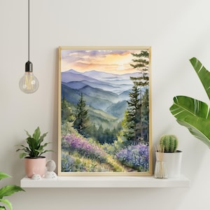 Pode incluir: Pintura em aquarela emoldurada de uma paisagem de montanha. A obra retrata camadas de montanhas azuis e verdes sob um c&eacute;u de p&ocirc;r do sol. Flores silvestres roxas e &aacute;rvores perenes est&atilde;o em primeiro plano.