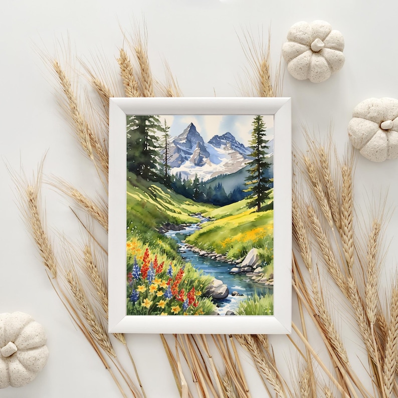 Op de afbeelding: Een aquarel schilderij van een berglandschap met een beek die door een vallei stroomt. De bergen zijn met sneeuw bedekt en de vallei is gevuld met wilde bloemen. Het schilderij is ingelijst in een wit frame.
