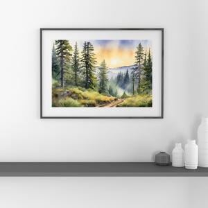 Op de afbeelding: Waterverf schilderij van een bospaadje dat naar een bergketen leidt met een zon die door de bomen schijnt. Het schilderij is ingelijst in een zwart frame.