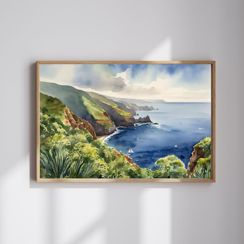 Op de afbeelding: Waterverfschilderij van een kustlandschap met groene heuvels en een diepblauwe oceaan. Een kleine zeilboot is zichtbaar in het water. Het kunstwerk is ingelijst in een lichtbruine houten lijst, wat een serene uitstraling cre&euml;ert.