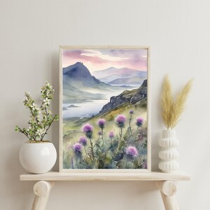以下が含まれることがあります： 水彩画で描かれた山岳風景画。前景には湖があり、空は淡いピンクとパープルで、山は濃いブルー。前景には紫色の野花が咲いている。