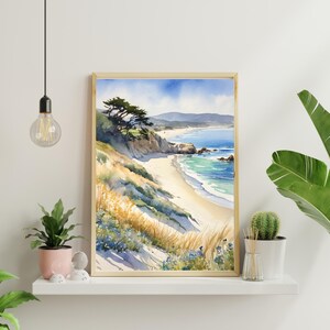 K&ouml;nnte beinhalten: Aquarellgem&auml;lde einer Strandszene mit einem Sandufer, blauem Meer und einem gr&uuml;nen Baum auf einer Klippe. Das Gem&auml;lde ist in einem hellen Holzrahmen gerahmt.