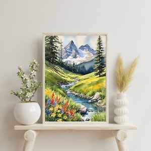 Op de afbeelding: Waterverf schilderij van een berglandschap met een beek die door een vallei stroomt. De bergen zijn met sneeuw bedekt en de vallei is gevuld met groen gras en wilde bloemen. Het schilderij is ingelijst in een licht houten lijst.