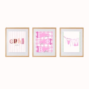 Peut inclure: Trois impressions encadrées avec des cadres en bois. Les impressions présentent des motifs roses et blancs. Une impression comporte les lettres "GPhi" avec du texte en dessous. Une autre impression présente des lettres grecques sur une bannière rose. La troisième impression montre de la lingerie rose suspendue à une corde à linge.