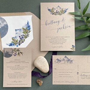 May include: A rustic wedding invitation suite with a watercolor mountain range and floral design. The invitation features the couple's names, "Brittany & Jackson", and the wedding date. The RSVP card includes a mountain range design and the text "Please reply no later than July 8th".