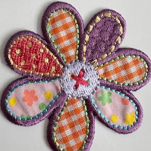 May include: A vibrant iron-on flower motif with a variety of patterned petals. The petals feature pink, orange gingham, and purple fabrics, with a light purple centre and a red cross-stitch. The product is labelled "Iron on Motif".