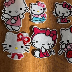 May include: Eight embroidered Hello Kitty patches in various designs. Each patch features the character with pink bows and accents. The patches are white, pink, red, and blue, with black outlines. The patches are ideal for customising clothing.
