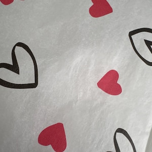 May include: White paper featuring a pattern of red and black outlined hearts. The hearts are distributed across the surface, creating a romantic design. The paper has a slightly textured appearance.