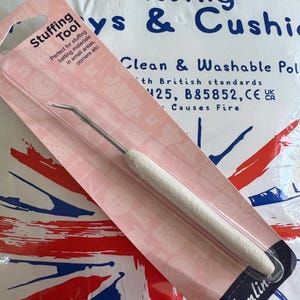 May include: A white stuffing tool in a pink package labelled "Stuffing Tool". The tool is for stuffing batting materials in small areas and corners. The package is on a bag with the Union Jack flag.