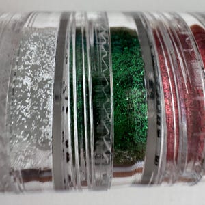May include: A clear plastic container filled with various colours of glitter. The glitter colours include silver, green, and red. The container is divided into separate compartments, each holding a different colour of glitter.
