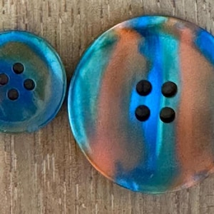 May include: Two round buttons with four holes each. The larger button has a diameter of approximately 3.8 cm, and the smaller button is about 1.9 cm. The buttons feature a swirl of blue, orange, and green colours.