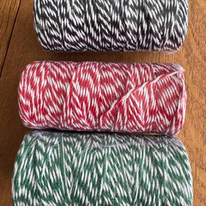 May include: Three spools of twine in black and white, red and white, and green and white chevron patterns. The twine is tightly wound, ideal for crafts or gift wrapping.