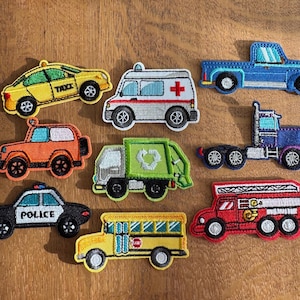 May include: A selection of embroidered vehicle patches, including a taxi, ambulance, truck, fire engine, police car, school bus, and a refuse truck. The patches are in various colours such as yellow, orange, red, blue, green, and black.