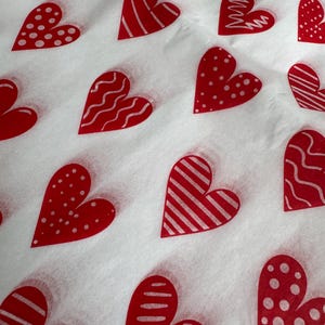 May include: A repeating pattern of red hearts on a white background. The hearts feature different designs, such as stripes, dots, and wavy lines. The design is evenly spaced across the surface.