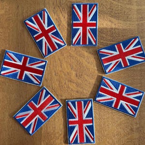 May include: Seven rectangular Union Jack flag patches arranged in a circle. Each patch has a blue border, a red cross, and white diagonal stripes. The patches are displayed on a wooden surface.