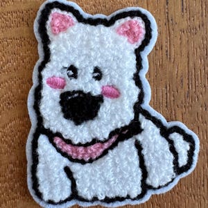 May include: White, textured bear patch with black outline and details. The bear has pink ears, cheeks, and a pink collar. The patch is on a light blue background.