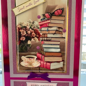 May include: A handmade birthday card with a layered design. The card features a stack of books, a teacup, and a bouquet of flowers. The text "Sent with Love" and "Happy Birthday" are included. The card has a pink and gold colour scheme.