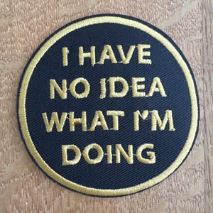 May include: A circular black patch with gold embroidered text: "I HAVE NO IDEA WHAT I'M DOING." The patch has a gold border. Suitable for sewing onto clothing or accessories.