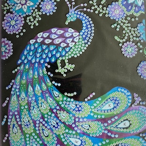 May include: A black diamond painting kit with a peacock design. The peacock is depicted with a vibrant blue, green, and purple tail, body and head. Floral accents in blue and purple surround the peacock.