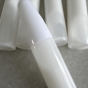 May include: Several white, cylindrical bottles with white conical caps are displayed. The image is a close-up, with one bottle in sharp focus, highlighting the smooth, glossy finish. The background is a neutral, light grey surface.