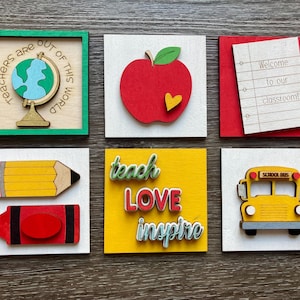 May include: A collection of six wooden school-themed decorations. Includes a globe in a green frame with the text "Teachers are out of this world", a red apple, a notepad with "Welcome to our classroom!", a pencil, a crayon, the words "teach love inspire", and a school bus.
