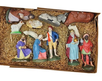 May include: A vintage nativity scene set with multiple figurines, including Mary, Joseph, baby Jesus, the three wise men, and animals. The figures are painted in various colors and set in a cardboard box filled with straw.