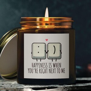 May include: A brown glass candle with a gold lid. The label features a cartoon image of two computer keys with faces, holding hands. The text on the label reads "Happiness is when you're right next to me."