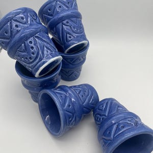 Könnte beinhalten: Eine Ansammlung von fünf blauen Keramikbechern mit einem erhabenen geometrischen Muster aus Dreiecken und Punkten. Jeder Becher hat eine glänzende Oberfläche und einen weißen Innenrand. Die Becher sind in einer Gruppe angeordnet.