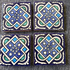 Könnte beinhalten: Vier quadratische Keramikuntersetzer mit einem sich wiederholenden geometrischen Design. Die Untersetzer haben einen dunkelblauen Hintergrund mit einem weißen, teal- und hellblauen Muster. Das Design ist symmetrisch und aufwendig, mit einem blütenartigen Zentrum.