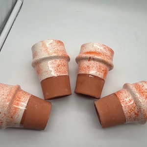Könnte beinhalten: Vier kleine Keramiktöpfe. Die Töpfe haben einen Terrakotta-Sockel und einen weißen oberen Bereich mit orangefarbenen Sprenkeln. Die Töpfe haben eine einzigartige, leicht ausgestellte Form.