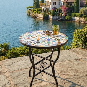 Può includere: Un tavolo da bistrot rotondo con un piano in mosaico colorato caratterizzato da motivi geometrici nei toni del blu, verde, arancione e bianco, sostenuto da una struttura in metallo nero con gambe curve e un decoro centrale a volute.