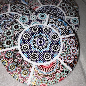 Könnte beinhalten: Ein Stapel dekorativer Untersetzer mit aufwendigen, farbenfrohen Mosaikmustern. Die Untersetzer haben ein kreisförmiges Design mit einem zentralen Motiv, das von segmentierten, gemusterten Abschnitten umgeben ist. Farben: Blau, Rot, Grün und Gold.