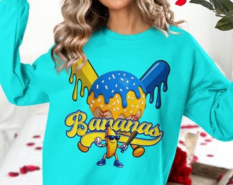 May include: Turquoise sweatshirt with a baseball-themed graphic. The design features a baseball with blue icing, a banana character holding a bat, and the word "Bananas" in yellow script.