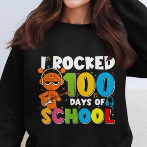 May include: A black sweatshirt with the text "I rocked 100 days of school" in colorful letters. A cartoon character with orange skin and headphones is playing a guitar.
