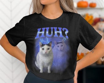 May include: Black t-shirt featuring a white and black cat with the word "HUH?" in blue, outlined in white. The cat is set against a blue background with lightning bolts. The shirt is a crew neck.