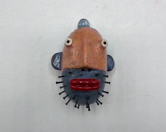 small round wall sculpture - orange person w/blue nail beard