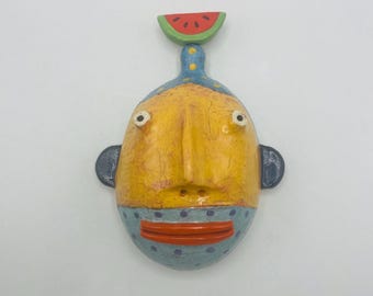 Escultura mural de media cabeza: persona barbuda con adorno de sandía.