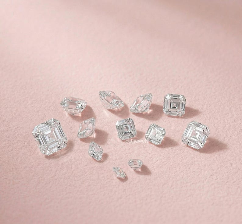 May include: A collection of clear, faceted diamonds of various shapes and sizes, scattered on a soft pink surface. The diamonds include emerald cuts and other geometric forms, reflecting light and creating a sparkling effect.