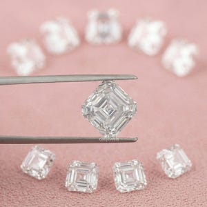 May include: A collection of Asscher cut diamonds, one held by tweezers, with others scattered on a pink surface. The diamonds are clear and reflect light, showcasing their intricate facets. The image is well-lit, highlighting the clarity and brilliance of the gemstones.
