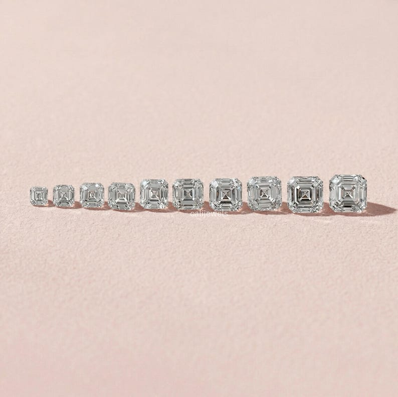May include: A collection of Asscher-cut diamond gemstones of varying sizes, arranged in a row on a light pink surface. The diamonds are clear and reflect light, showcasing their square shape with cut corners and step-cut facets.