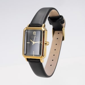 May include: A rectangular gold-coloured wristwatch with a black face and black leather strap. The watch has a gold bezel and a black leather strap with a buckle. The watch face has gold hands and a logo.