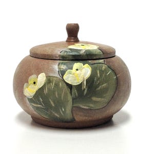 Peut inclure: Un petit pot rond en céramique brune avec un couvercle. Le pot est décoré de fleurs jaunes et de feuilles vertes peintes à la main.
