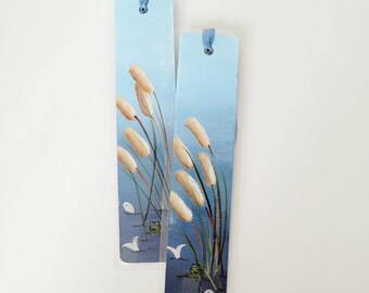 May include: Two blue and white painted bookmarks with a design of white reeds and green frogs. The bookmarks have blue ribbon ties.